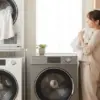 洗濯機とガス衣類乾燥機「乾太くん」、電気ヒートポンプ式洗濯乾燥機が並んだ明るいランドリールームで、乾燥後のふわふわなタオルを笑顔で抱きしめる日本人女性